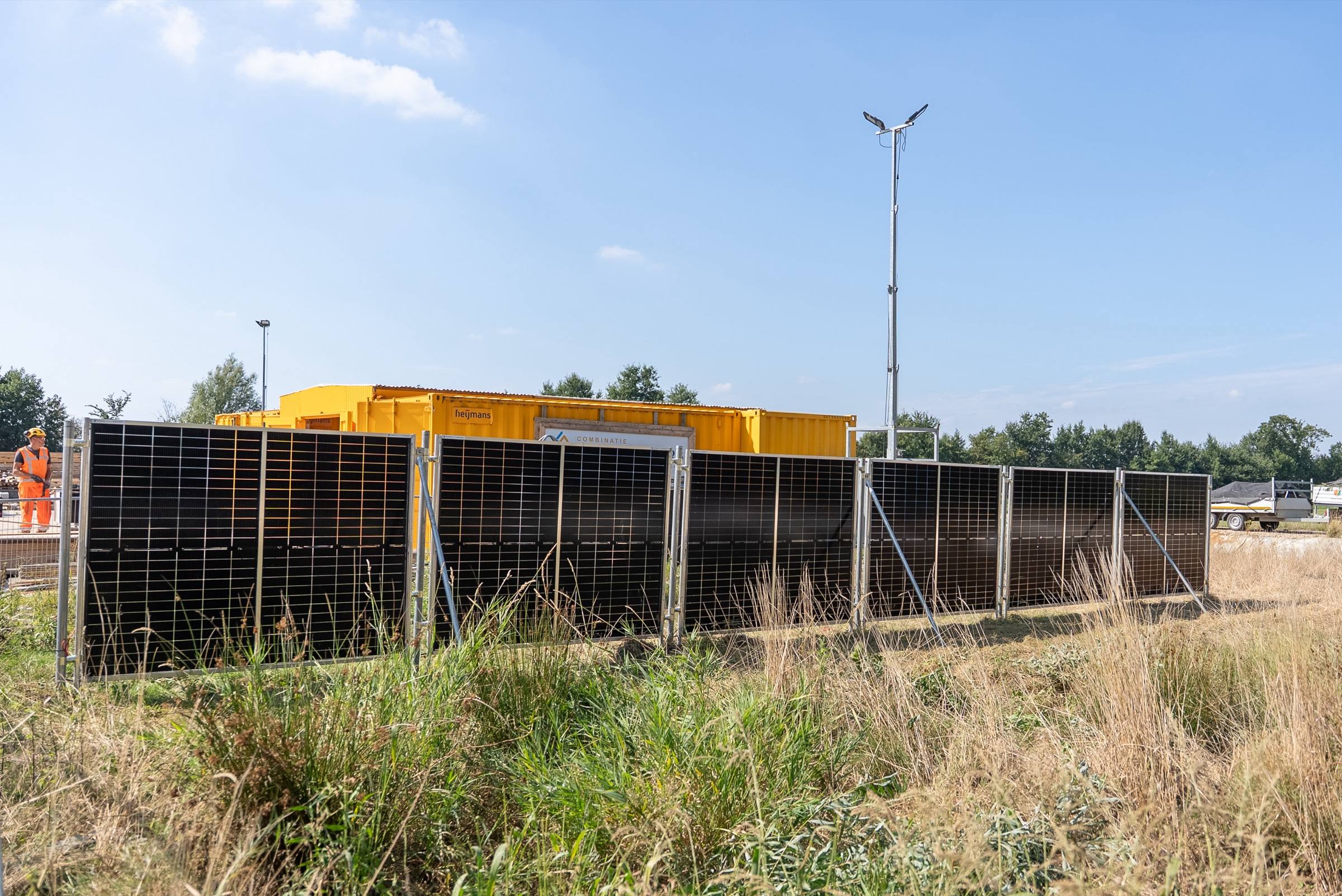 Rij zonnebouwhekken voor gele bouwcontainers en een lichtmast