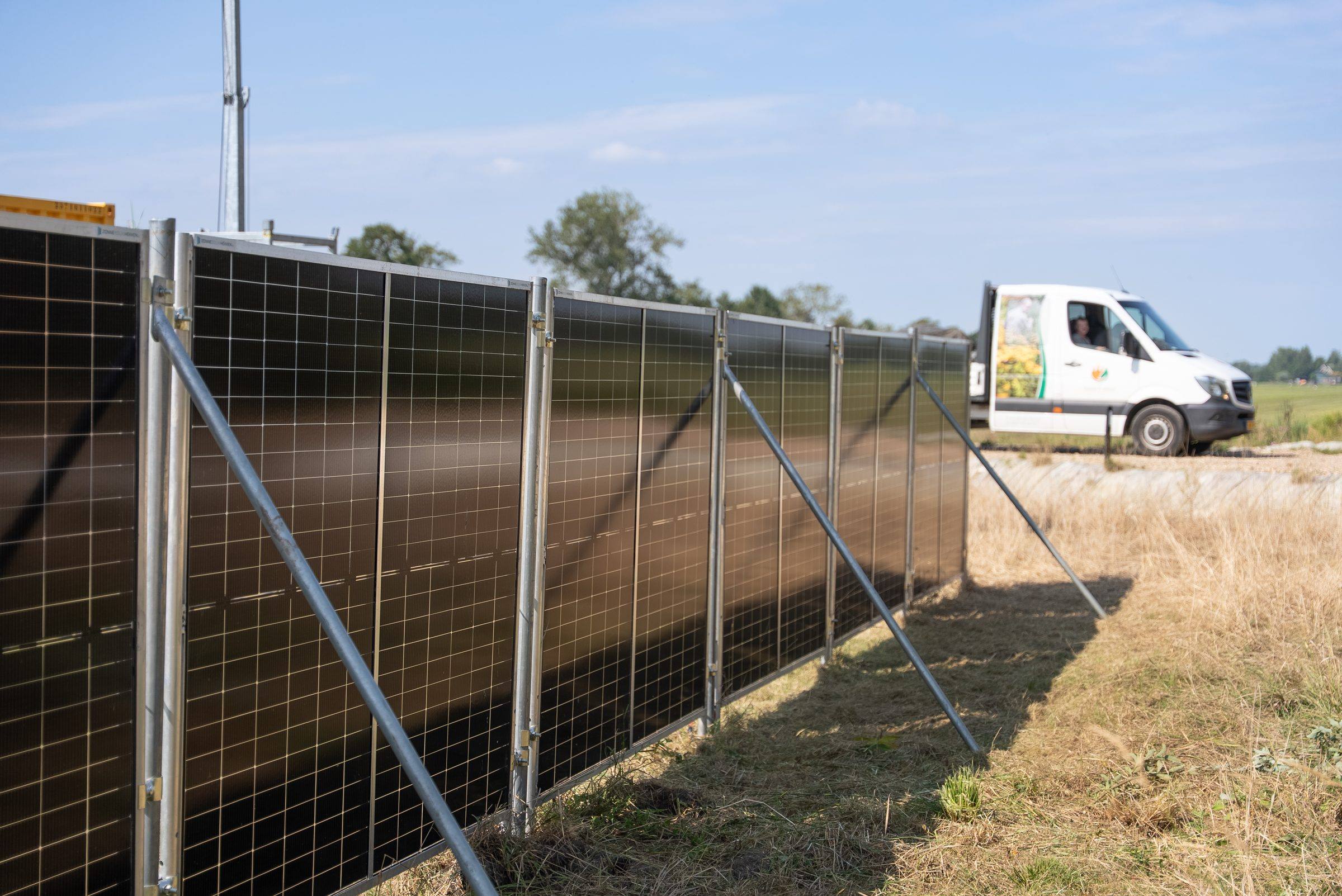 Een rij zonnebouwhekken met zonnepanelen langs een bouwterrein, met een bedrijfsbus van Green to Grow