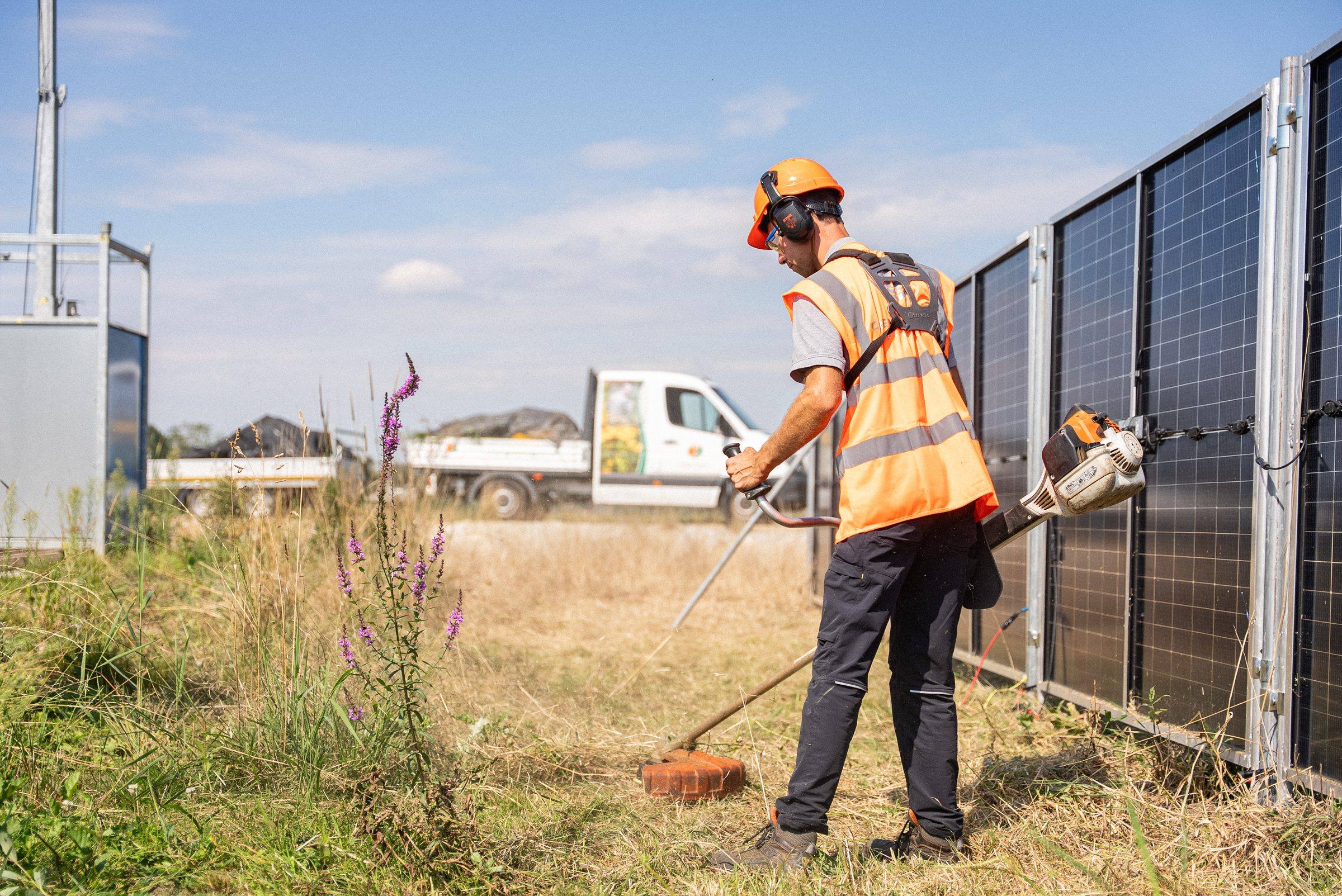 Medewerker maait het gras langs de zonnebouwhekken