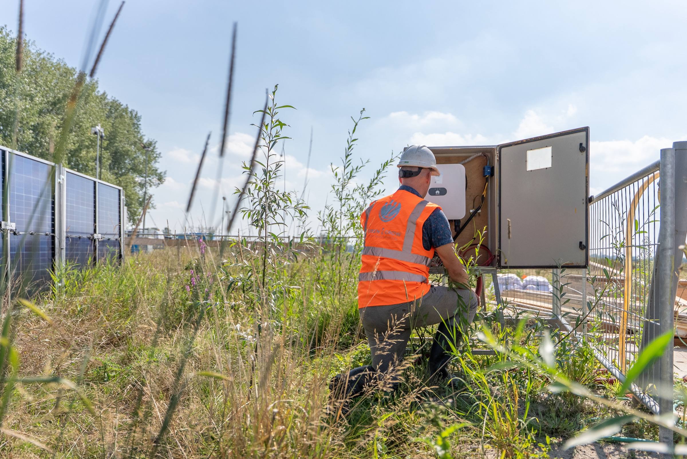 Monteur sluit de omvormerkast aan naast een rij zonnebouwhekken op een bouwterrein