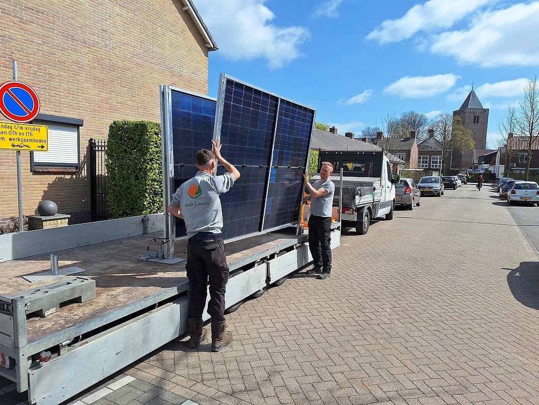 Twee medewerkers plaatsen een zonnebouwhek vanaf een aanhanger in de dorpsstraat bij Ons Huys